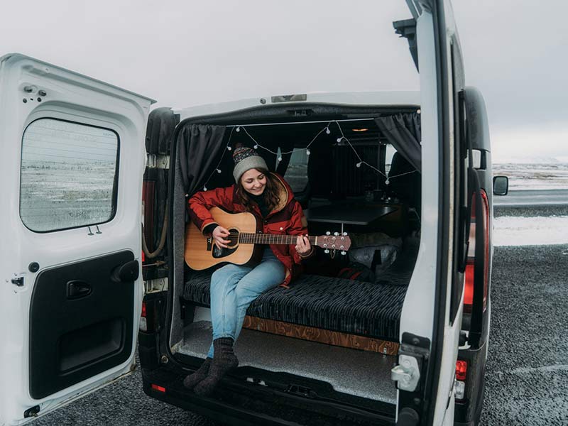 Young woman playing guitar in camper van in Iceland