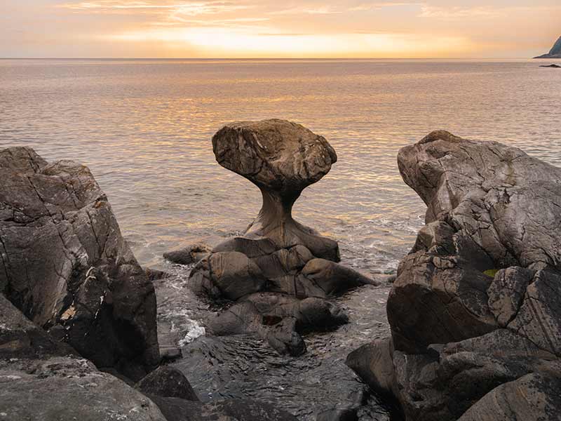 Stone with unusual form at the shore in Norway with sunset in the background
